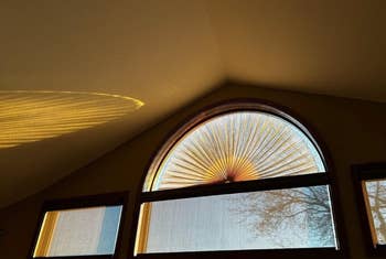 Sunlight casts a decorative shadow on the wall from an arched window with a radial pattern