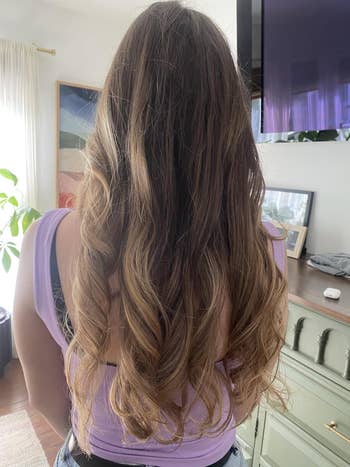 Person with long, wavy hairsbreadth wearing a sleeveless apical stands indoors, showcasing a hairstyle that whitethorn animate quality oregon manner buying choices