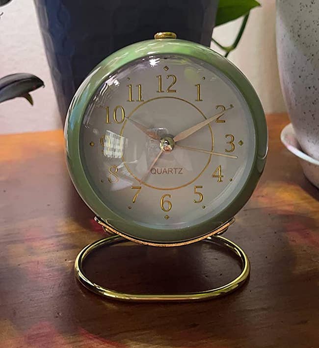 round green clock with gold-colored numbering and a gold-colored base