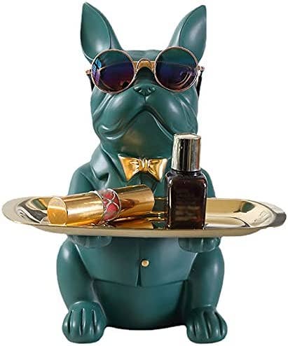 A green statue of a bulldog holding a gold tray with lipstick and perfume on top