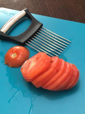 Sliced tomato laid out on a blue cutting board with a wavy slicer knife beside it