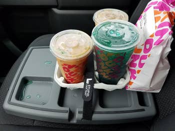 Three different drinks on a car cup holder tray next to a fast-food bag, showcasing beverage options for a shopping decision