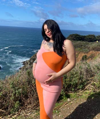 reviewer in a fitted maternity dress standing near a coastline