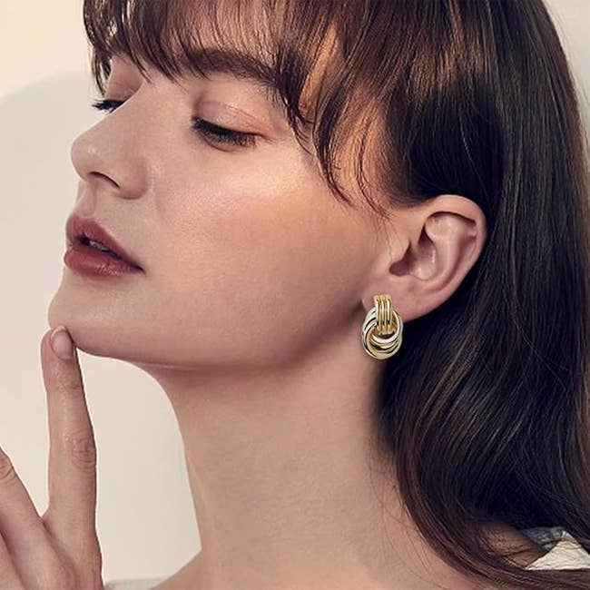 model with agelong  hairsbreadth  wearing knot-shaped earrings, looking thoughtful with eyes closed, touching her chin