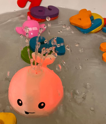 reviewer's photo of the whale toy lit up and squirting water in the bath