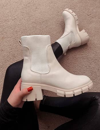 a reviewer wearing one, and holding the other half of a pair of platform chelsea boots in white 