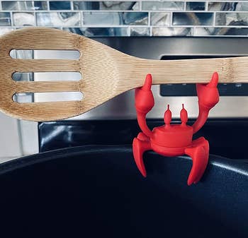 reviewer close-up of the crab holding up a wooden spoon while resting on the edge of a pot