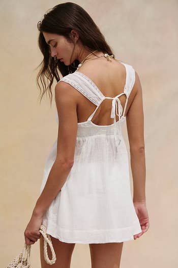 Person in a sleeveless, lace-trimmed sundress carrying a woven bag, facing away, in a shopping-inspired setting