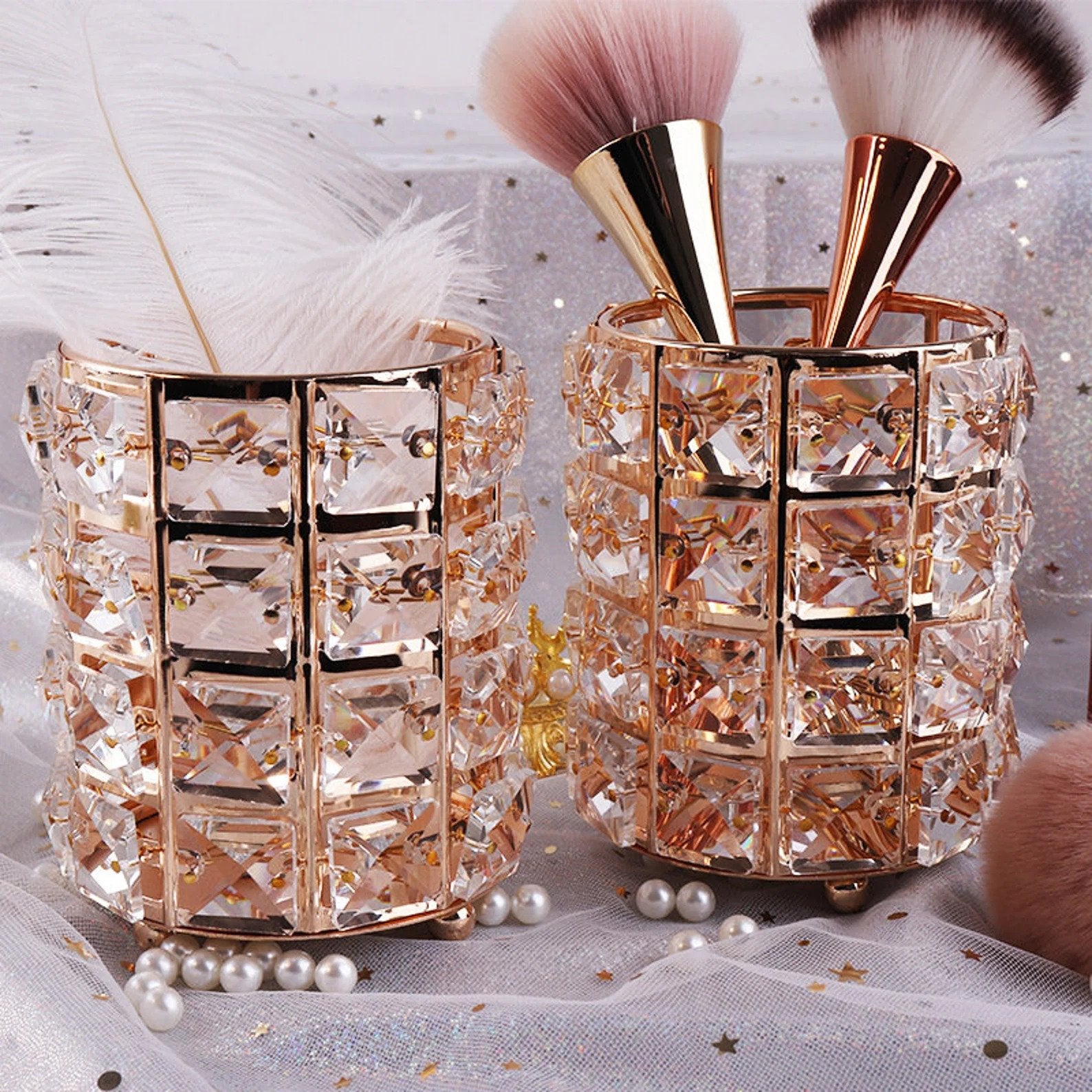 Two pink crystal pencil cups with gold metal square in between. The cups are holding make up brushes