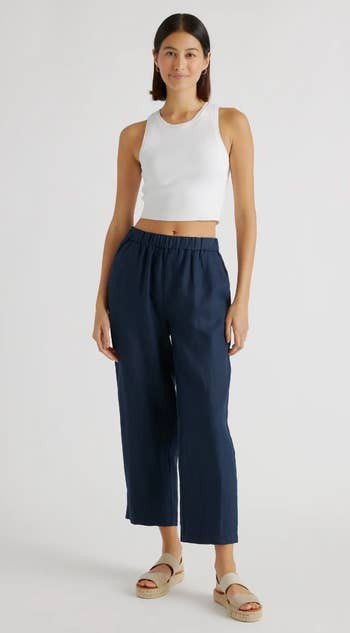 Model showcasing a white sleeveless top with navy blue cropped trousers and beige sandals
