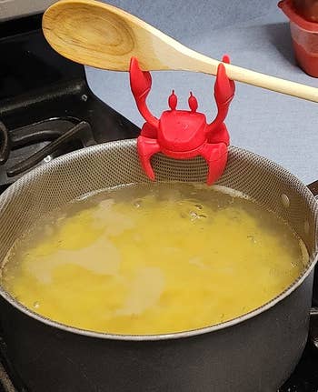 reviewer photo of the crab attached to the rim of a pot filled with water and pasta while holding up a wooden spoon