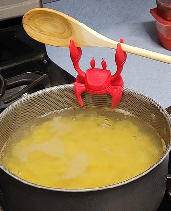 reviewer photo of the crab attached to the rim of a pot filled with water and pasta while holding up a wooden spoon