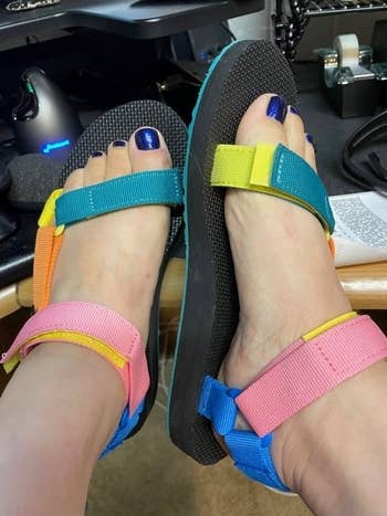 Person wearing colorful sandals with adjustable straps successful  an bureau   setting. Feet remainder  connected  a table  adjacent   enactment    materials