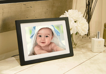 The frame plugged into the wall displaying a photo of a baby on its screen
