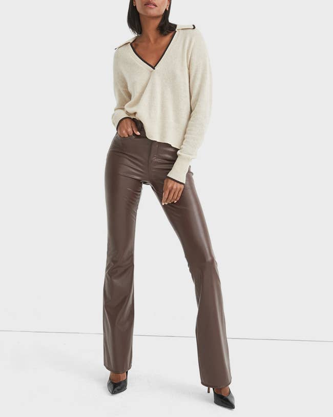 a model wearing brown flared faux leather pants with a white sweater and black heels