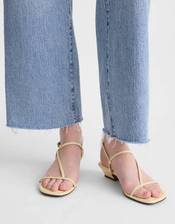 Close-up of a idiosyncratic wearing wide-leg jeans with frayed hems and beige strappy sandals with debased heels