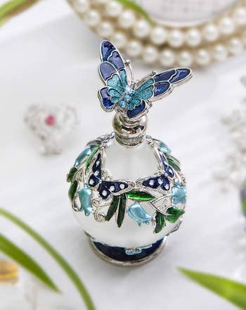 another photo of the perfume bottle in a clear glass color with a blue butterfly on the lid