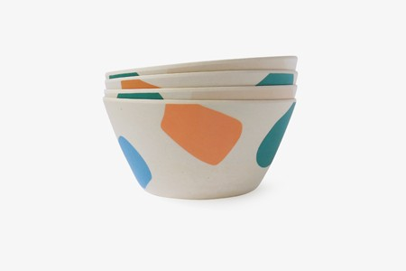 Four bowls with green, orange, and blue abstract shapes stacked together on a white background