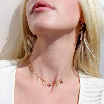 a model wearing a gold initial necklace with charms that spell 