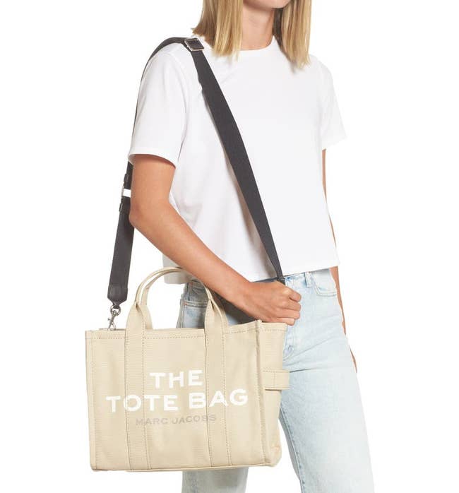 a model holding the beige bag with a black strap