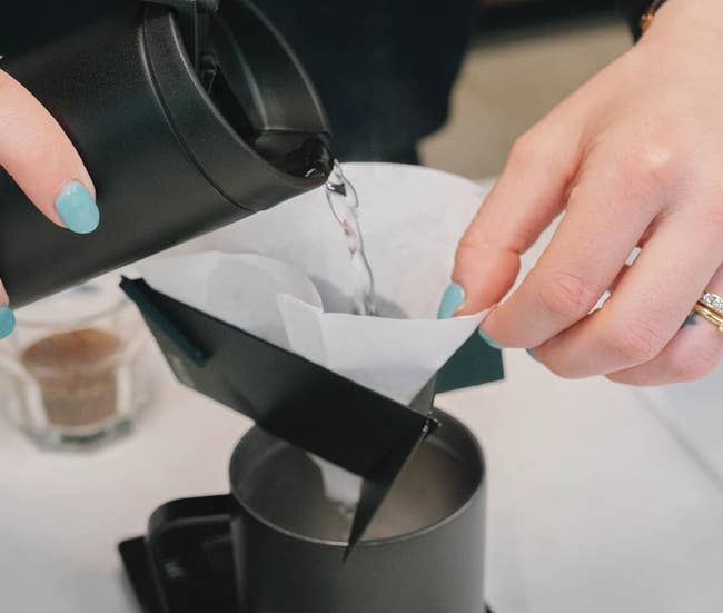 Reviewer using a matte black folded device to pour hot water into a mug 