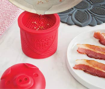 bacon grease being poured into the red bacon bin, which is next to a plate of bacon