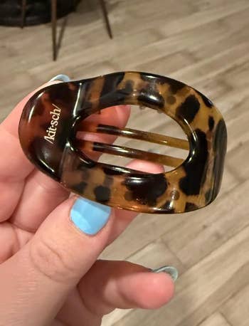 Hand holding a tortoiseshell-patterned hair clip by Kitsch, showing its oval shape and sturdy design, suitable for styling accessories