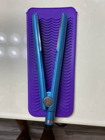 Reviewer photo of their blue flat iron resting on top of a purple silicone mat