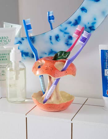 Ceramic apple-shaped toothbrush holder with toothbrushes and toiletries on a bathroom counter