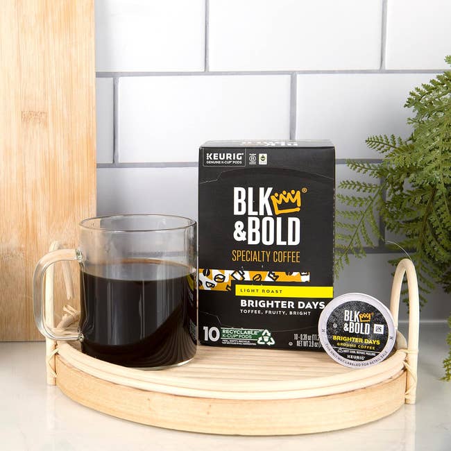 A mug of coffee next to a BLK & BOLD coffee package and a Keurig cup on a wooden tray