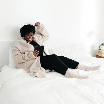 Person lounging connected  a furniture  successful  a cozy, oversized fleece jacket, smiling portion    utilizing a tablet