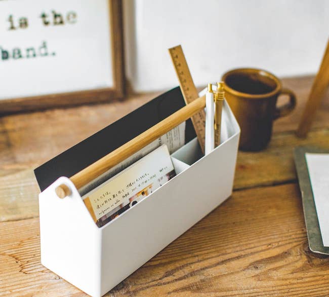 a white desk organizer with an attached wooden handle filled with various office supplies 