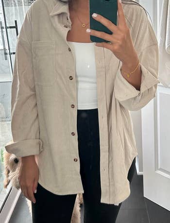 Person in a casual button-up shirt and black pants taking a mirror selfie, focusing on outfit details for shopping inspiration