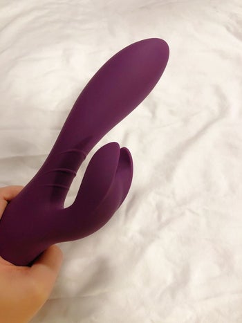 Hand holding purple rabbit vibrator to display kneading clitoral arm
