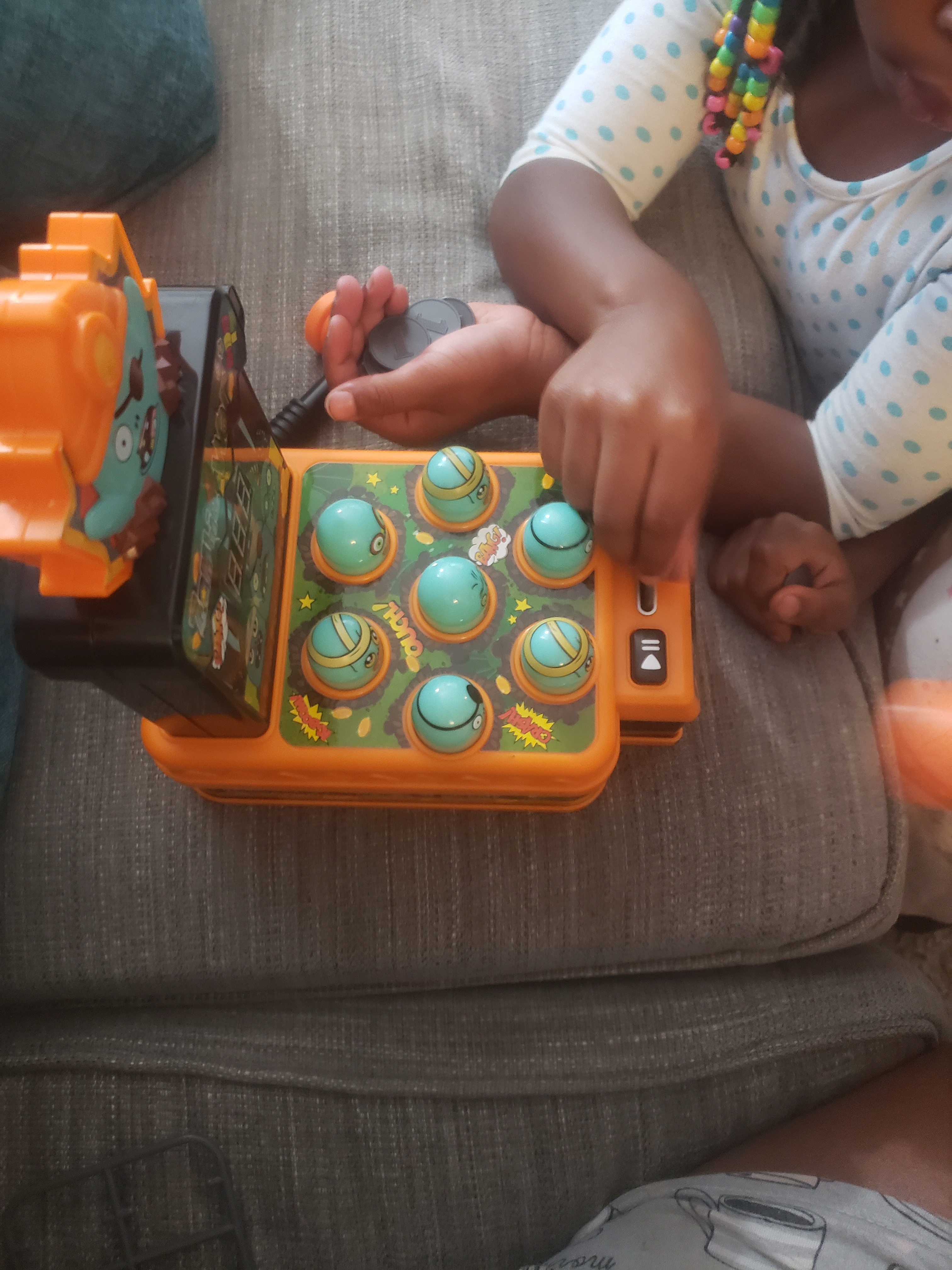 Child playing with a artifact  resembling a whack-a-mole crippled  connected  a couch
