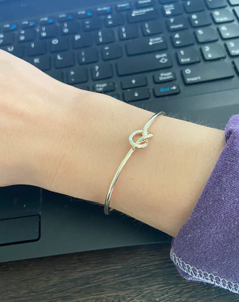 Reviewer wearing thin gold band with a subtle knot at the top on their wrist 
