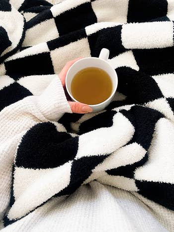 another reviewer with the black and white throw blanket in lap while holding cup of tea