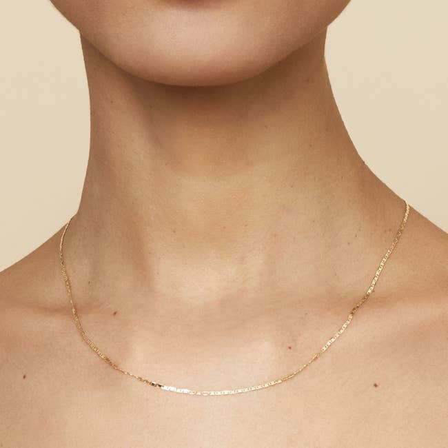a model wearing a thing gold chain necklace