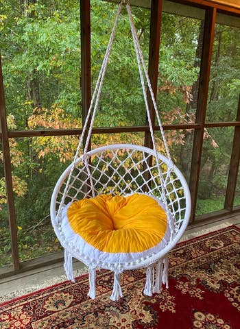 Reviewer image of white macrame chair hanging with an orange and white cushion