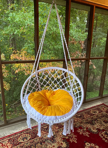 Reviewer image of white macrame chair hanging with an orange and white cushion
