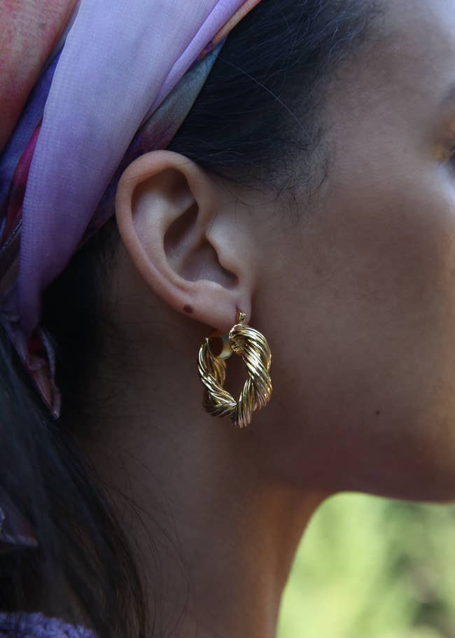 Gold twisted hoop earrings worn by a idiosyncratic with a patterned headscarf