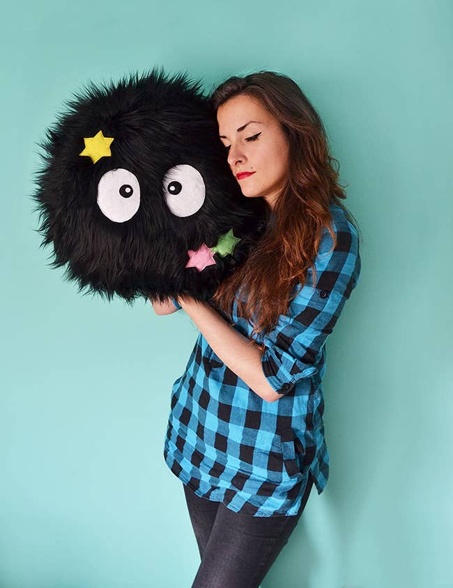 model holding fluffy soot sprite plush with stars on it that's about three times the size of their head