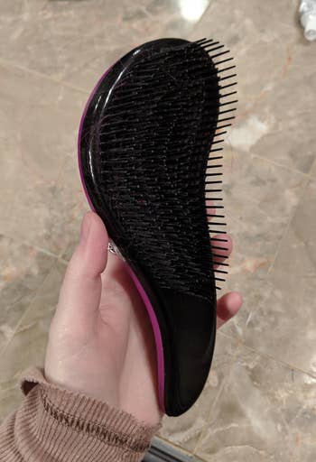 A detangling brush with a shape that curves similar to an 'S' shape. It has bristles along the entire surface.
