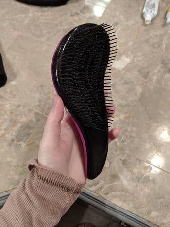 A reviewer holding a detangling brush with a shape that curves similar to an 'S' shape. It has bristles along the entire surface.
