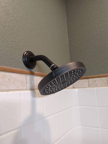 reviewer image of the round bronze shower head installed in a shower