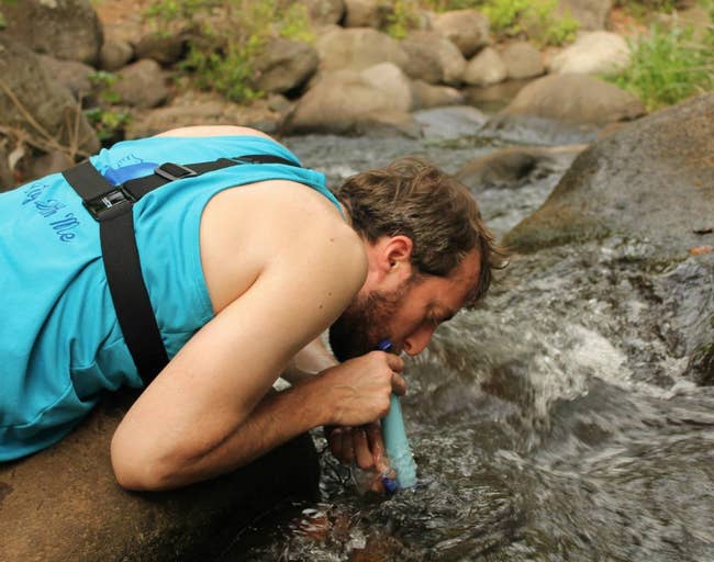 Reviewer drinking water from a river using the lifestraw