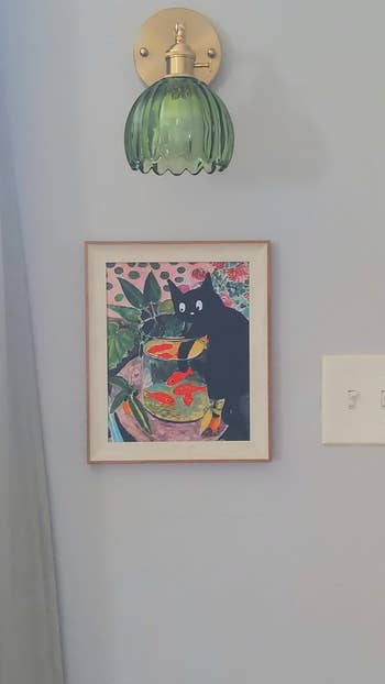 Framed artwork of a achromatic  feline  playfully interacting with goldfish successful  a bowl, hanging beneath  a decorative airy  fixture connected  a wall