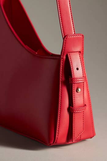 Close-up of a red leather handbag with a focus on the strap and stitching detail