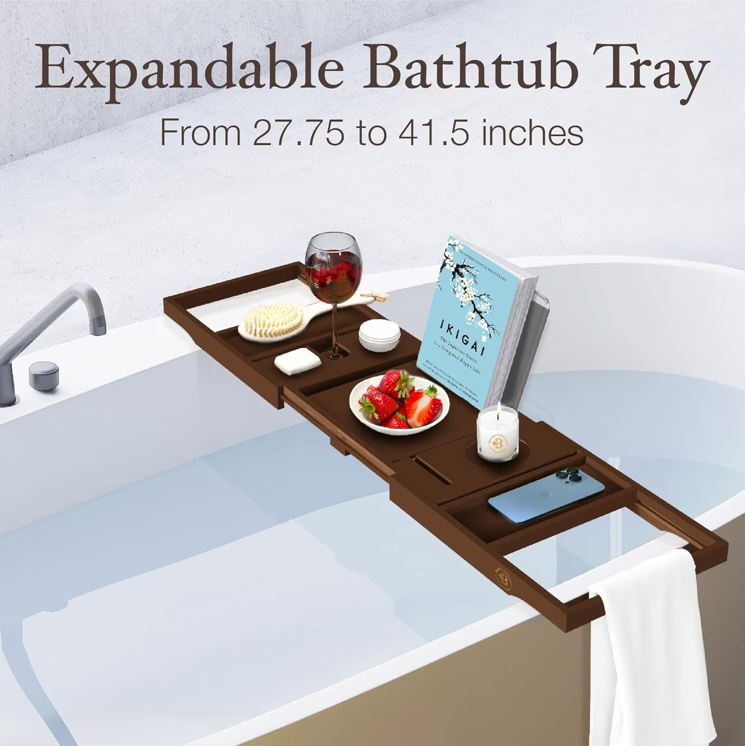 Expandable bathtub tray holding wine, a book, fruit, and bath items, extends from 27.75 to 41.5 inches