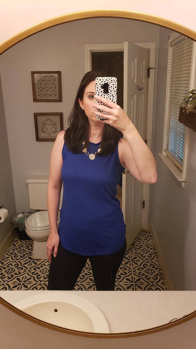 Reviewer in a sleeveless blue top and black pants taking a selfie in mirror